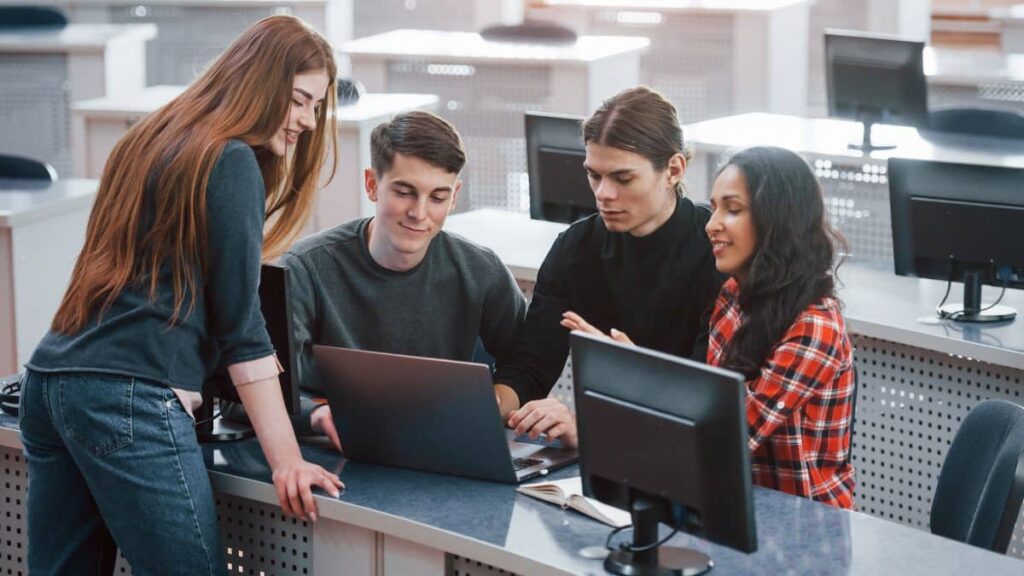 Quatro estudantes discutindo projetos em um laboratório de informática.