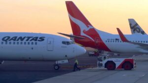 Aeronaves da Qantas Airways estacionadas no aeroporto ao entardecer, destacando a expansão da companhia aérea com voos de longa duração.