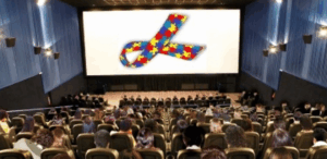 Sessão especial para autistas em cinema com público e símbolo do autismo na tela, promovendo inclusão e acessibilidade.