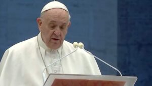Papa Francisco recebe alta e aparece em discurso após internação, usando vestes papais diante de microfone em cerimônia oficial.