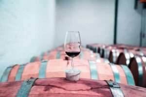 Taça de vinho tinto sobre barril de madeira em adega, ilustrando tema sobre se vinho tinto faz bem para a saúde.