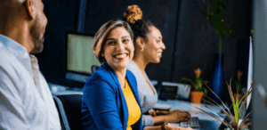 Três profissionais trabalhando em escritório moderno, sorrindo e demonstrando bem-estar durante o expediente