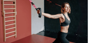 Mulher praticando exercício físico com fita de suspensão, fortalecendo a musculatura em ambiente de academia