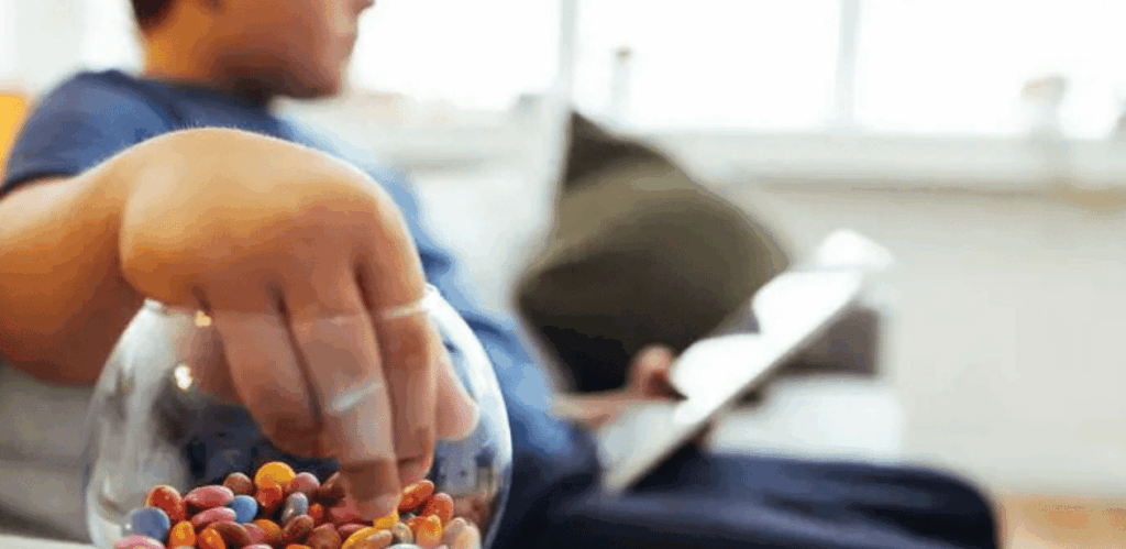 menino brincando no sofa com um tablet e comendo doce.