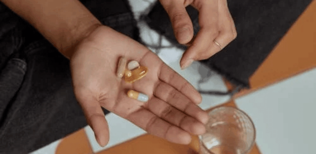 Pessoa segurando cápsulas e comprimidos na mão, representando suplemento de vitamina D para esclerose múltipla.