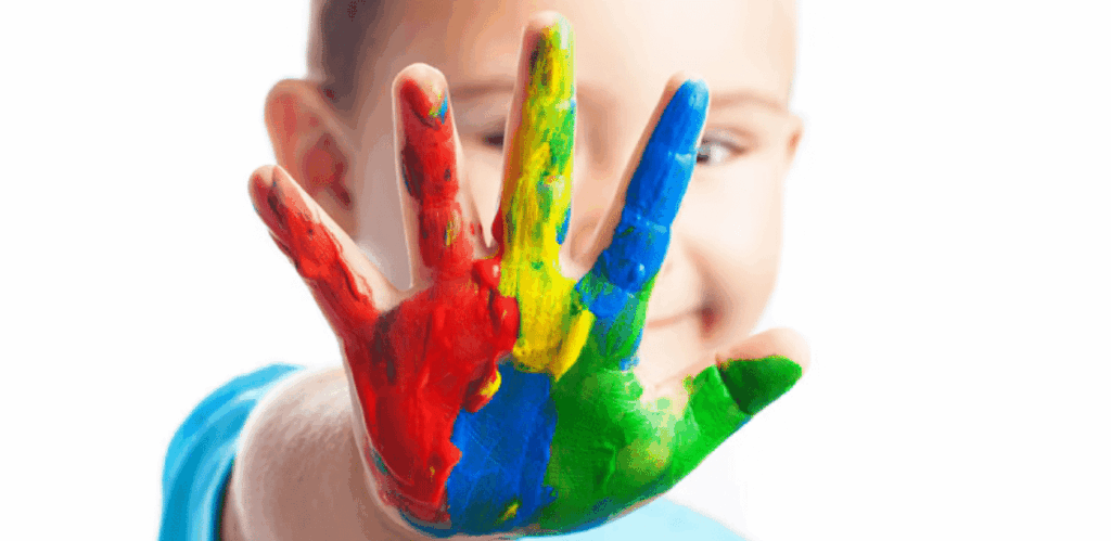 Criança com a mão pintada de cores do autismo simbolizando inclusão e criatividade no Dia Mundial de Conscientização sobre o Autismo