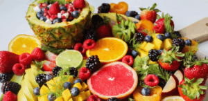Variedade colorida de frutas ricas em fibras, como morango, laranja, framboesa, kiwi e abacaxi, dispostas sobre uma tábua.