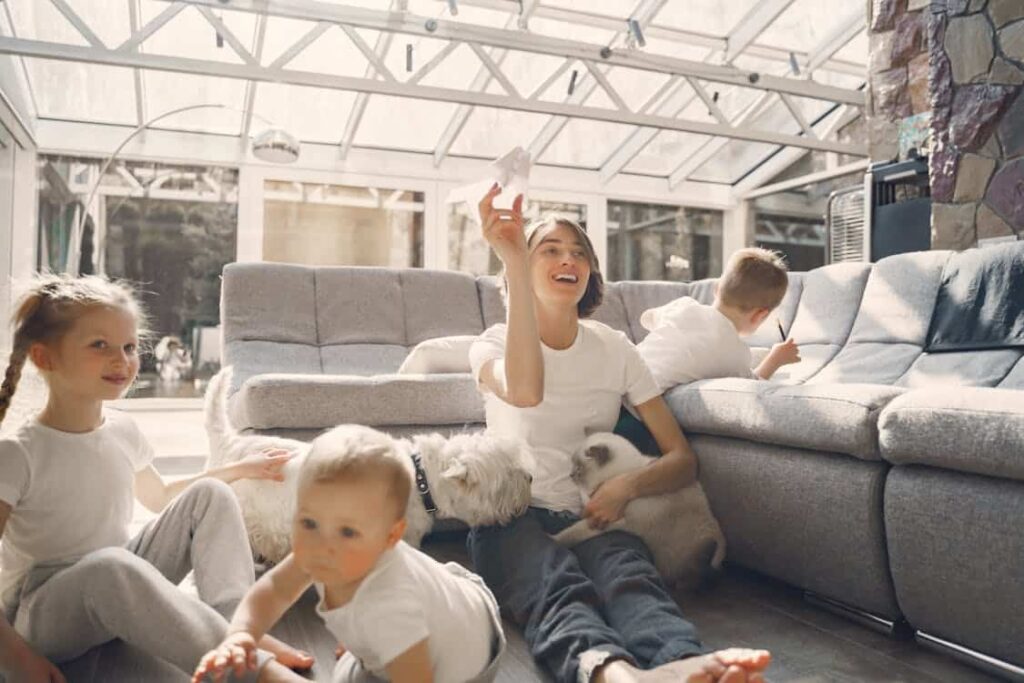 Família com crianças brincando com cães e gato na sala, representando como pets aumentam o bem-estar e promovem convivência saudável.
