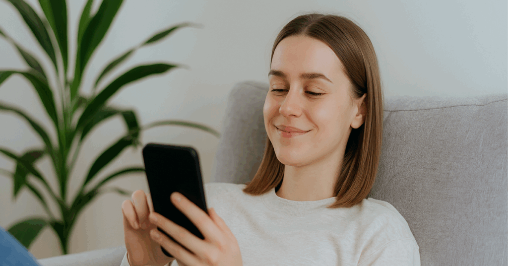 Jovem relaxa no sofá enquanto mexe no celular em ambiente iluminado