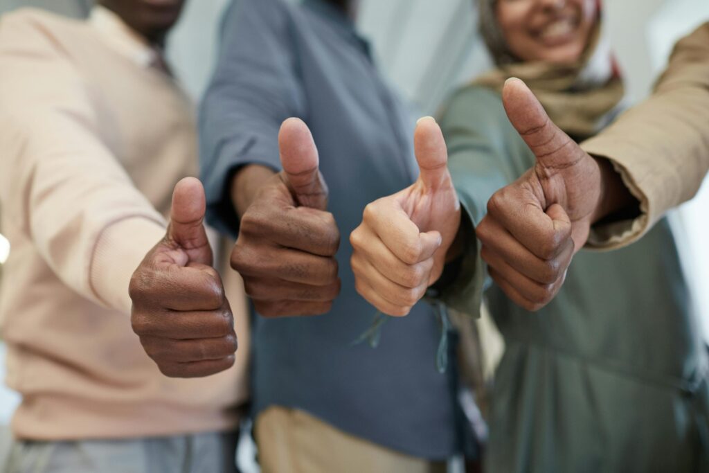 Grupo de pessoas fazendo o sinal de positivo com o polegar em direção à câmera, expressando otimismo e união.