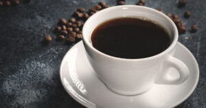 Xícara de café preto em fundo escuro com grãos ao redor